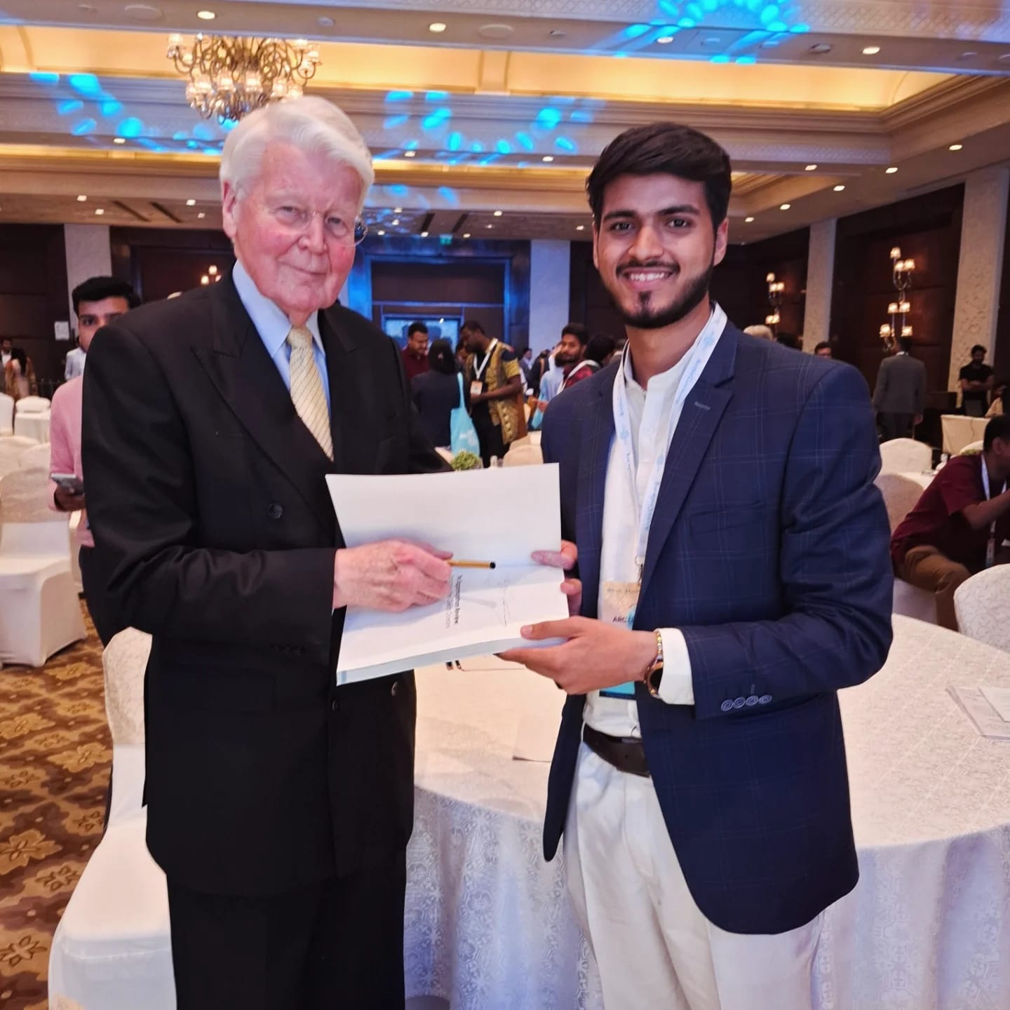 Akshat Mehrotra with a male dignitary, both holding a book.